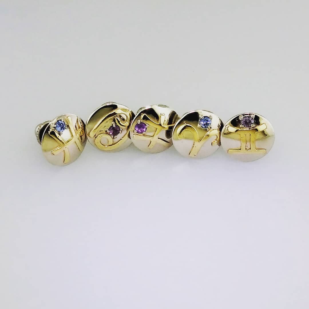 Sterling silver domed pins with 14k yellow gold zodiac symbols embellished with prong set birthstones.