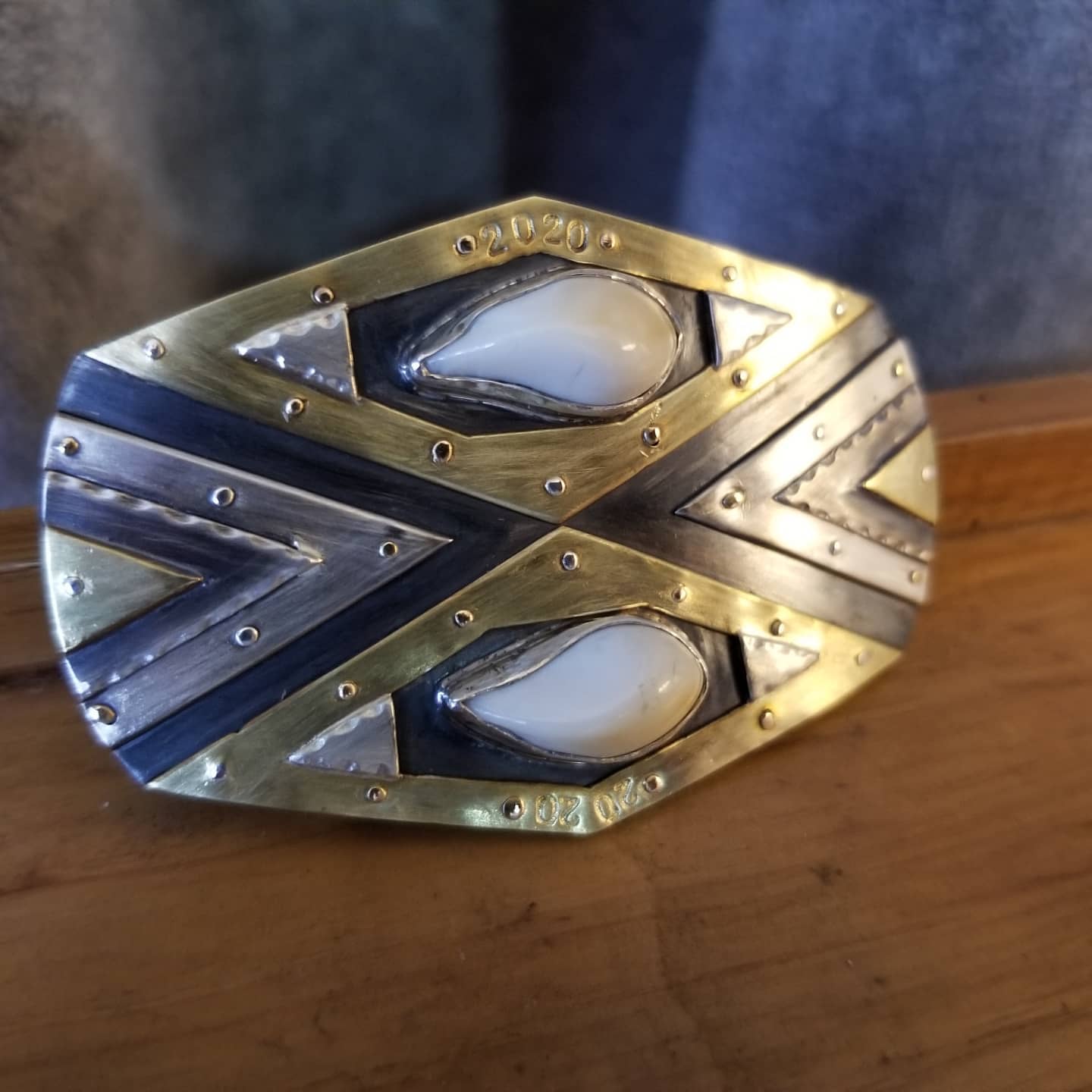 Sterling silver and brass layered belt buckle with bezel set elk teeth and decorative rivets.