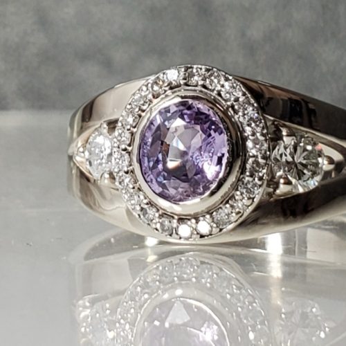 Oval purple sapphire bezel set in a halo of diamonds with side round diamonds on a split shank of 14k white gold. Made by Katherine Spencer in Morgantown, West Virginia USA