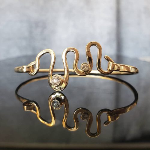 14k yellow gold hammer flattened squiggle crafted to be the hinge on a gold band, accented with bezel set round diamonds.