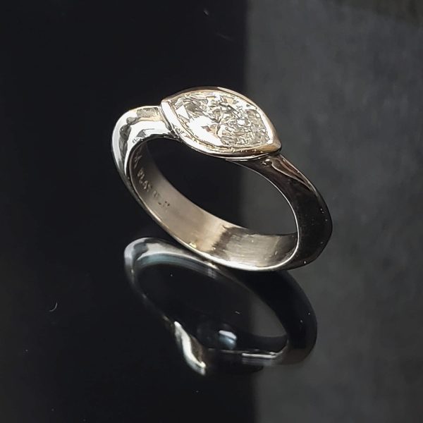 An east west placed marquise diamond is bezel set on a knife edge 14k white gold band, giving the engagement ring a fun touch of visual contrast. Item 1016