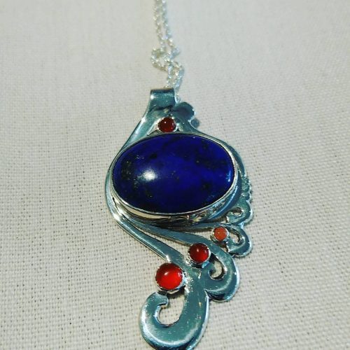 Blue lapiz cabochon bezel set in a sterling silver art nouveau inspired design with red carnelian accents.