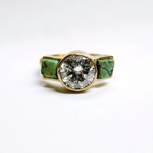 Round brilliant center diamond with turquoise cube side stones all bezel set in 18k yellow gold with a brush finish.