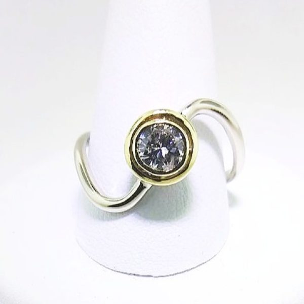 Center diamond bezel set in 18k yellow gold on a single twist 14k white gold band, certainly a unique "twist" on a classic engagement ring. Item 1003