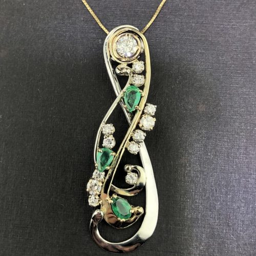 Pear shaped emeralds and round diamonds set in twists and vines with a bezel set round diamond at the top.