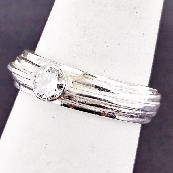This textured band is crafted of 14k white gold and holds a diamond in the center, engagement ring, round diamond. Item 1014