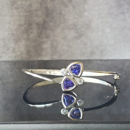 Two bezel set trillion purple tanzanites, with bezel set round diamonds on a 14k white gold hinge bracelet.