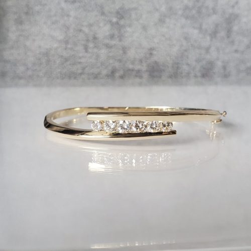 Overlapping 14k yellow gold bangle with pointed ends and channel set round diamonds in between.