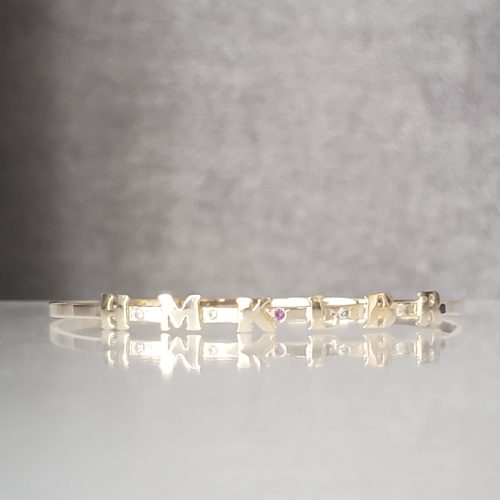 14k yellow gold, hand cut letters, on a gold bangle band with accented diamonds.
