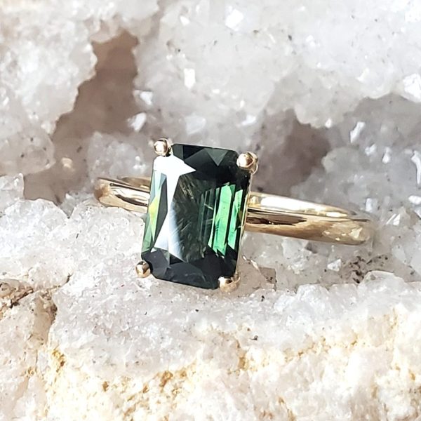 Emerald cut green stone, prong set on a thin 14k yellow gold band, a colorful twist on a classic style engagement ring. Item 1011