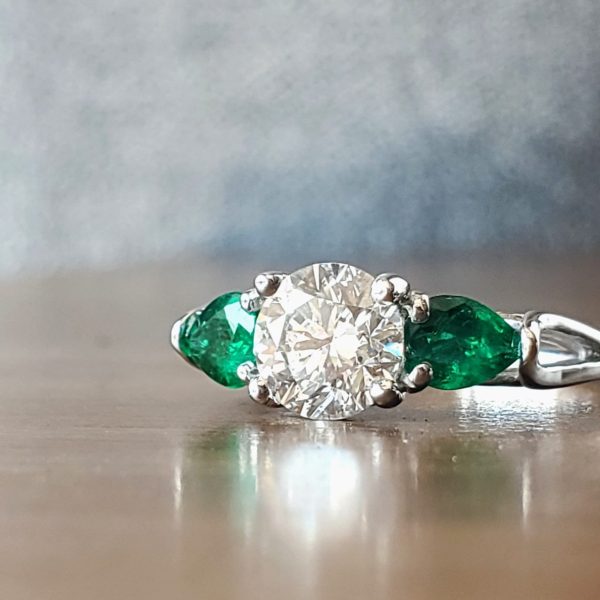 Three stone ring with a round brilliant center and pear shape emeralds prong set in a white gold woven basket setting