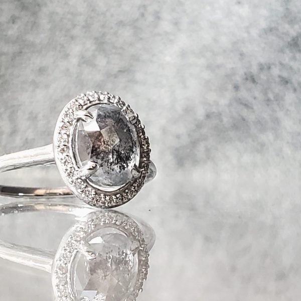 Oval rose cut salt and pepper diamond, with a white diamond halo on a 14k white gold band.