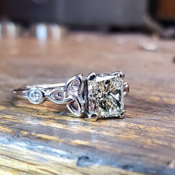 Emerald cut diamond prong set on a 14k white cathedral style gold band with Celtic tri-knots and round brilliant diamond accents