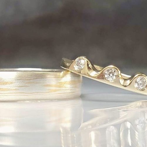 Men's 5mm half round wedding band in 22k yellow gold and sterling silver mokume gane. Ladies yellow gold crown style wedding band with flush set diamond accents. Created by Katherine Spencer. Made in Morgantown, West Virginia USA