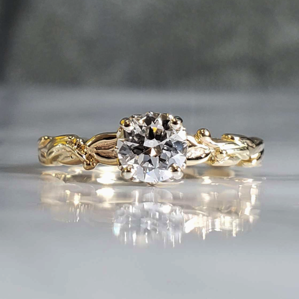 Bright white round diamond prong set on a 14k yellow gold band with leaf and vine carved accents.