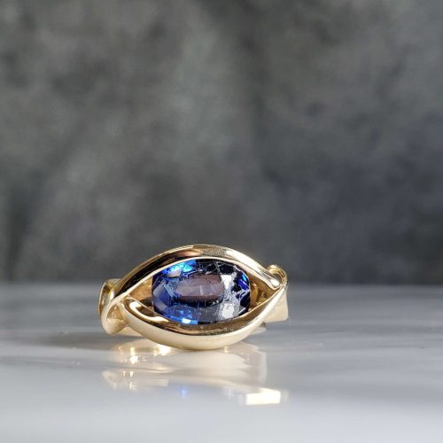 3ct. oval blue sapphire channel set in 14k yellow gold with side swirl accents. Created by Katherine Spencer. Made in Morgantown, West Virginia USA