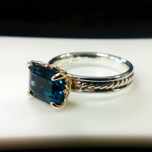 Princess cut ruby, prong set on a 14 yellow gold band with diamond baguette side accents.