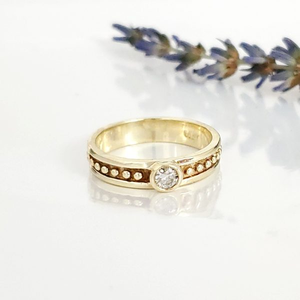 Bezel set diamond sits on a textured and beaded 14k yellow gold band, rustic engagement ring. Item 1013