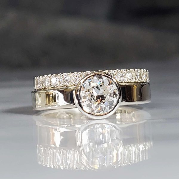 Classic, clean, simple lines. A platinum closed back bezel set diamond on a flat 14k white gold band. Shown with a 14 diamond French set white gold band.