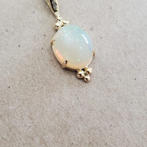 Shiny oval opal prong set with 14k yellow gold granulation details.