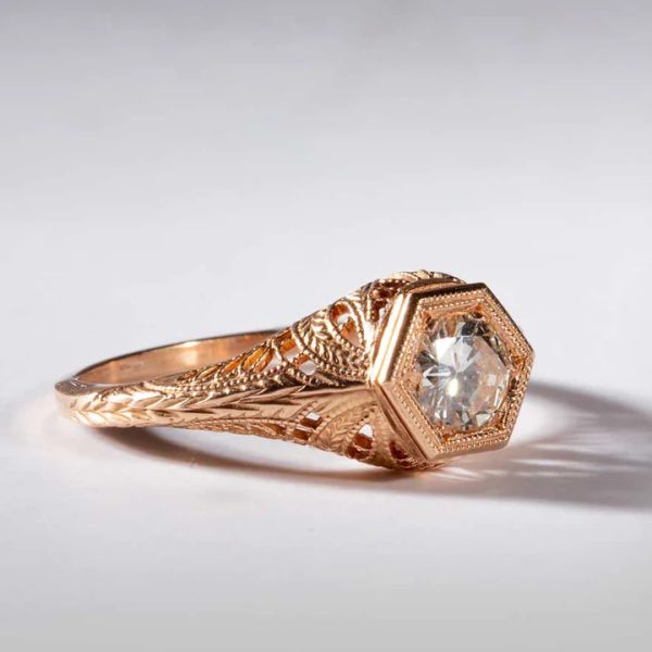 The intricate Laurel and Wheat patterns of this 1920's era filigree ring convey messages of honor and prosperity. The Hexagonal Head holding a 5mm gemstone is symbolic of harmony and balance. These design elements are typical of the period from which this ring first appeared and represent the epitome of craftsmanship and artistry.