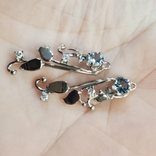 Hand fabricated 14k white gold leaves with bezel set round diamond details with a light blue round topaz on top.