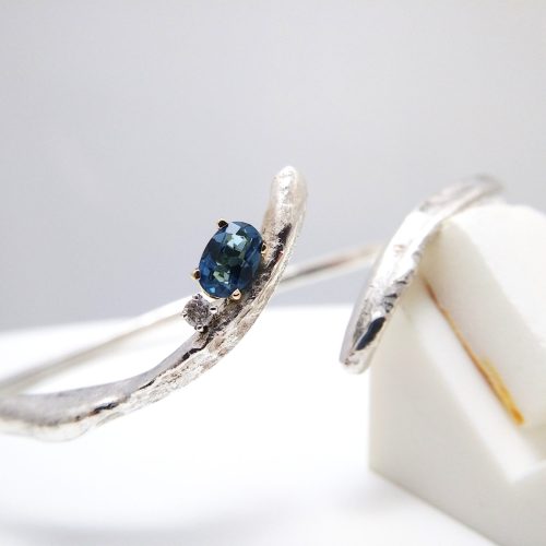 Molten open sterling silver open band with a prong set oval blue sapphire and diamond.