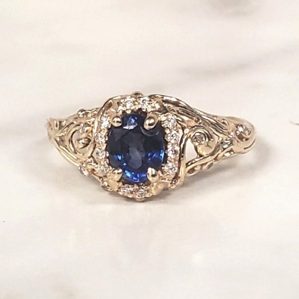 Oval blue sapphire set in 14k yellow gold on a filigree band with a diamond halo.