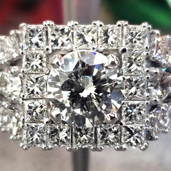 Round center diamond set in 14k white gold surrounded by a halo and rows of princess cut diamonds.
