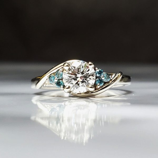 A bright white round diamond, centered on a 14k white gold bypass band with 3 dainty round blue diamonds on each side.