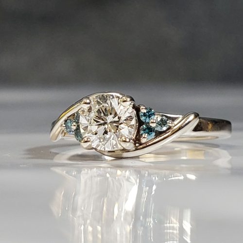 Twist style bypass engagement ring with a trio of blue diamond accenting a start 129 round diamond, set in 14k white gold. Created by Katherine Spencer. Made in Morgantown, West Virginia USA