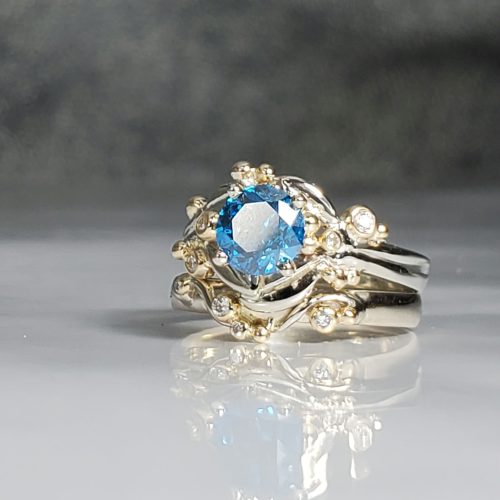 Leaf and Vine style engagement ring with a contour wedding band. 14k white and yellow gold rings with diamond accents, and a round blue diamond center. Designed and created by Katherine Spencer. Made in Morgantown, West Virginia USA